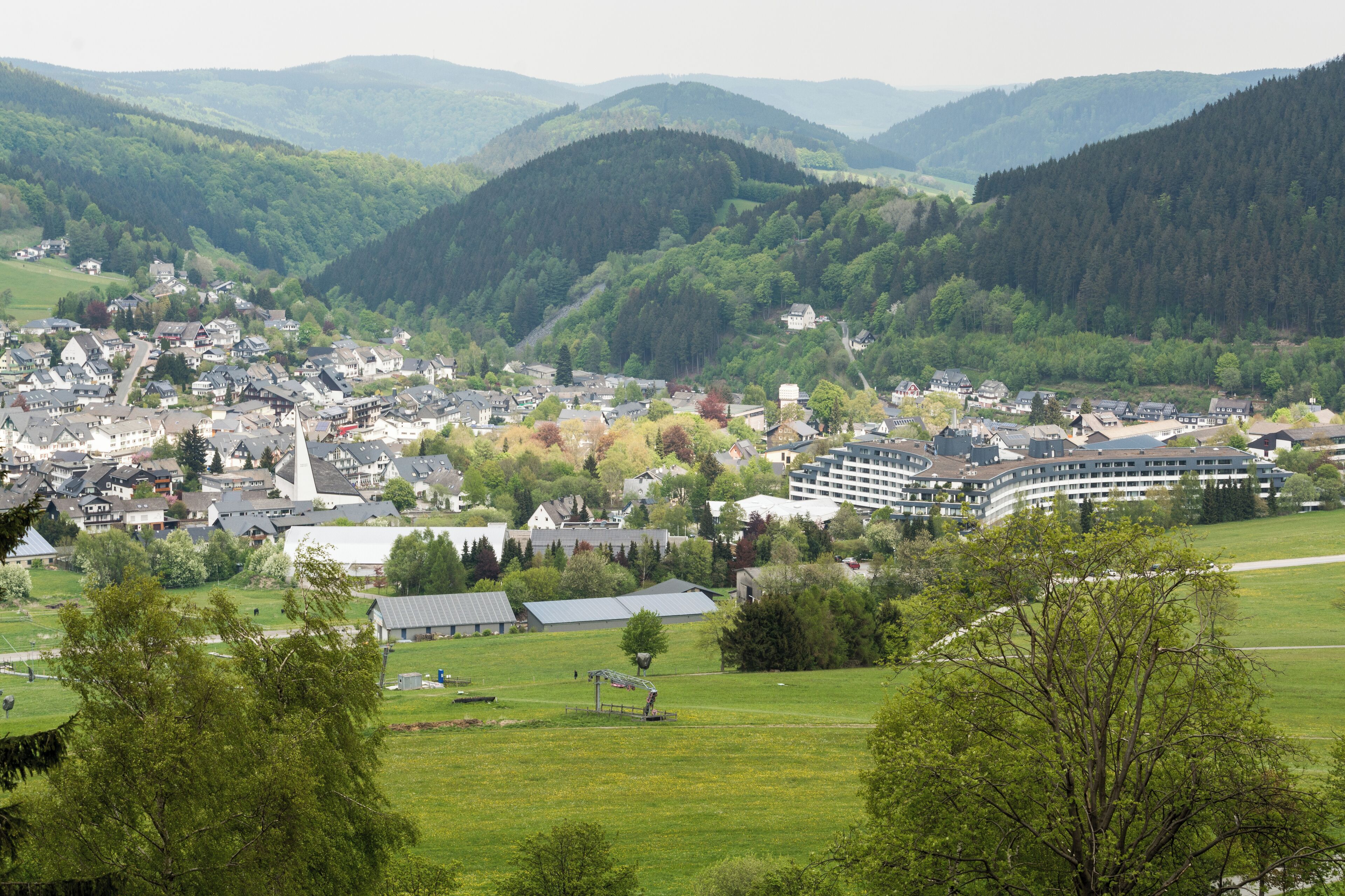 A town nestled in a valley with a prominent church, surrounded by lush green hills and a large hotel.
