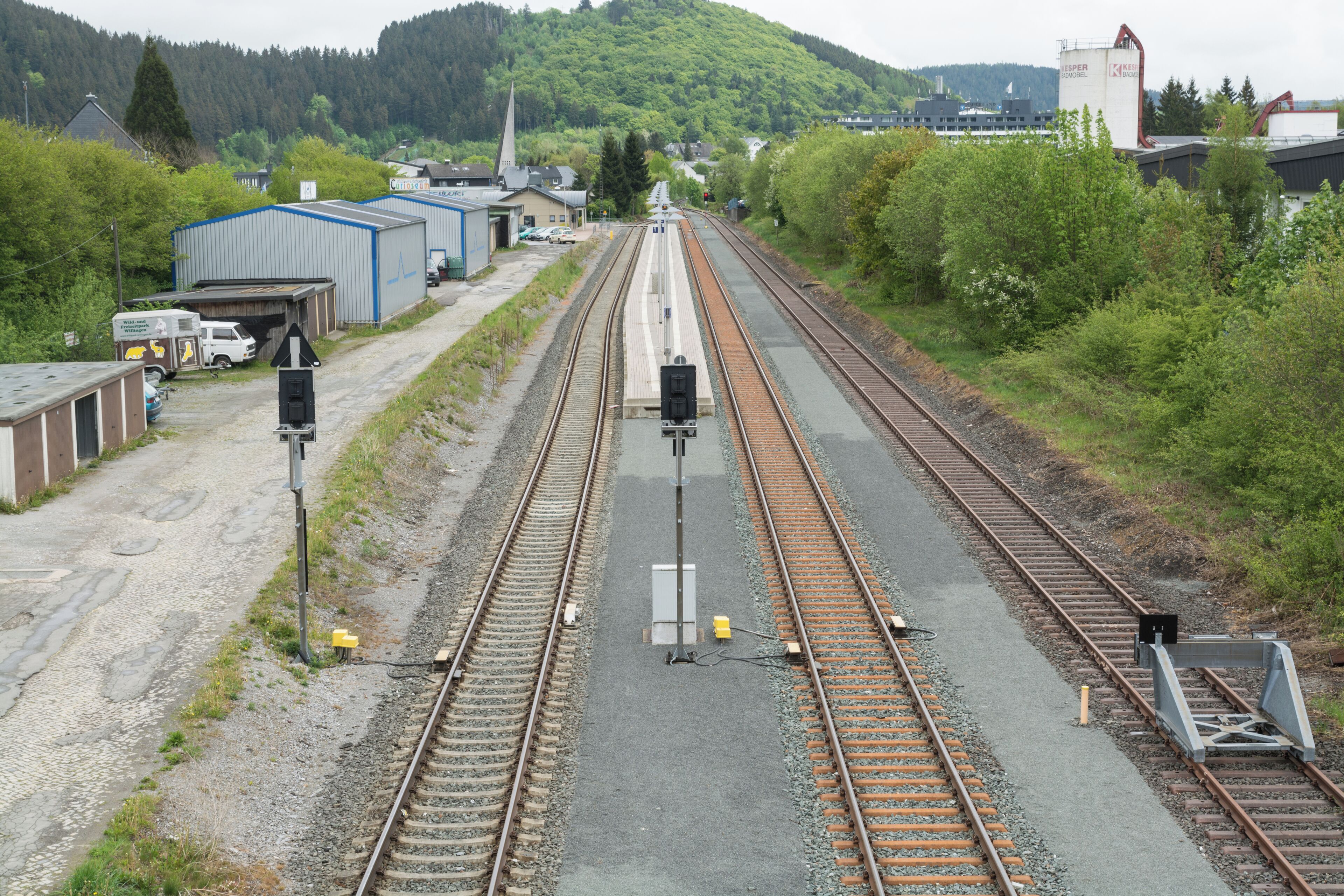 Railway tracks, a small station building, and a church steeple in a rural setting.
