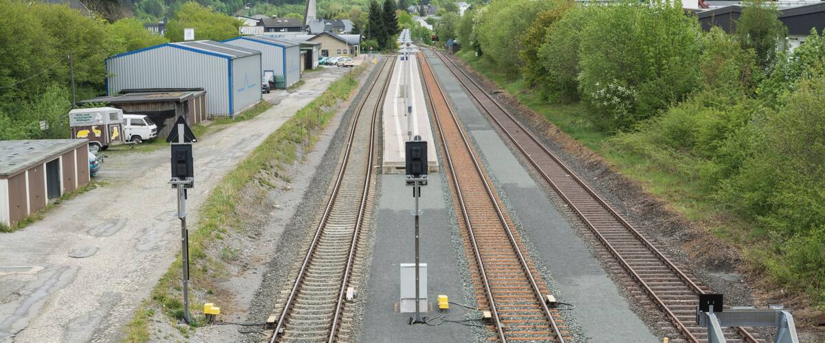 Railway tracks, a small station building, and a church steeple in a rural setting.
