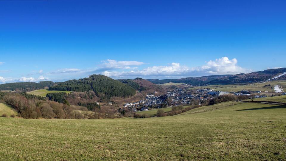A rural landscape with rolling hills, a small village, and a clear blue sky.