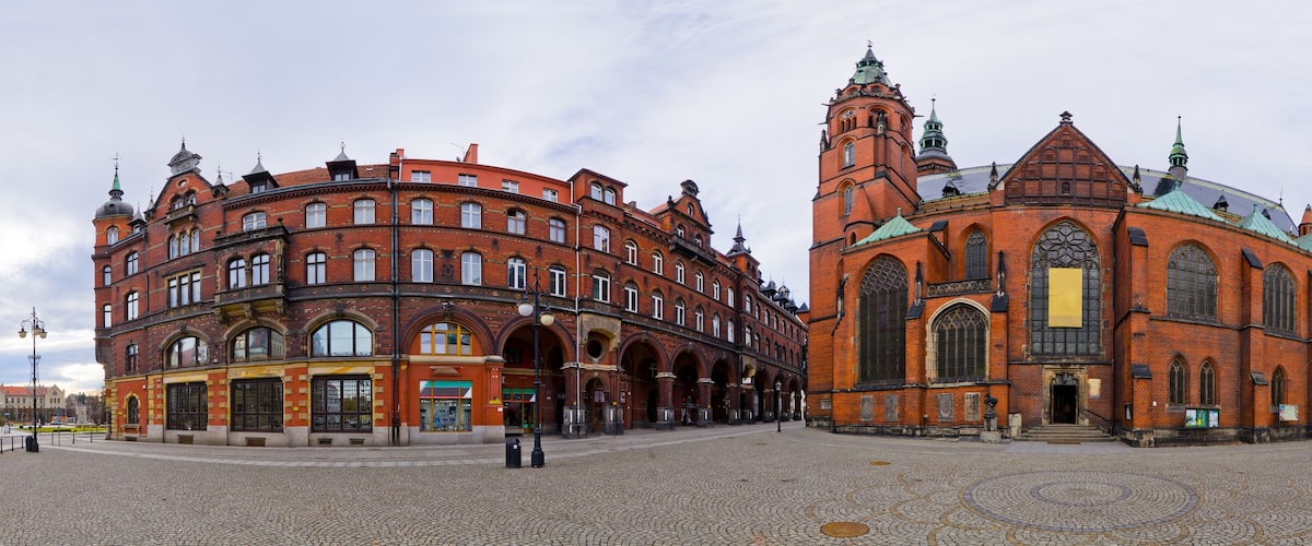 A historic square with cobblestone pavement, a prominent church with a green roof, and adjacent red-brick buildings.