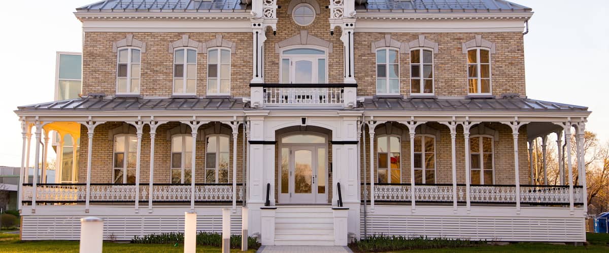A large, historic brick house with a symmetrical facade, a central entrance, and a covered porch with ornate railings.