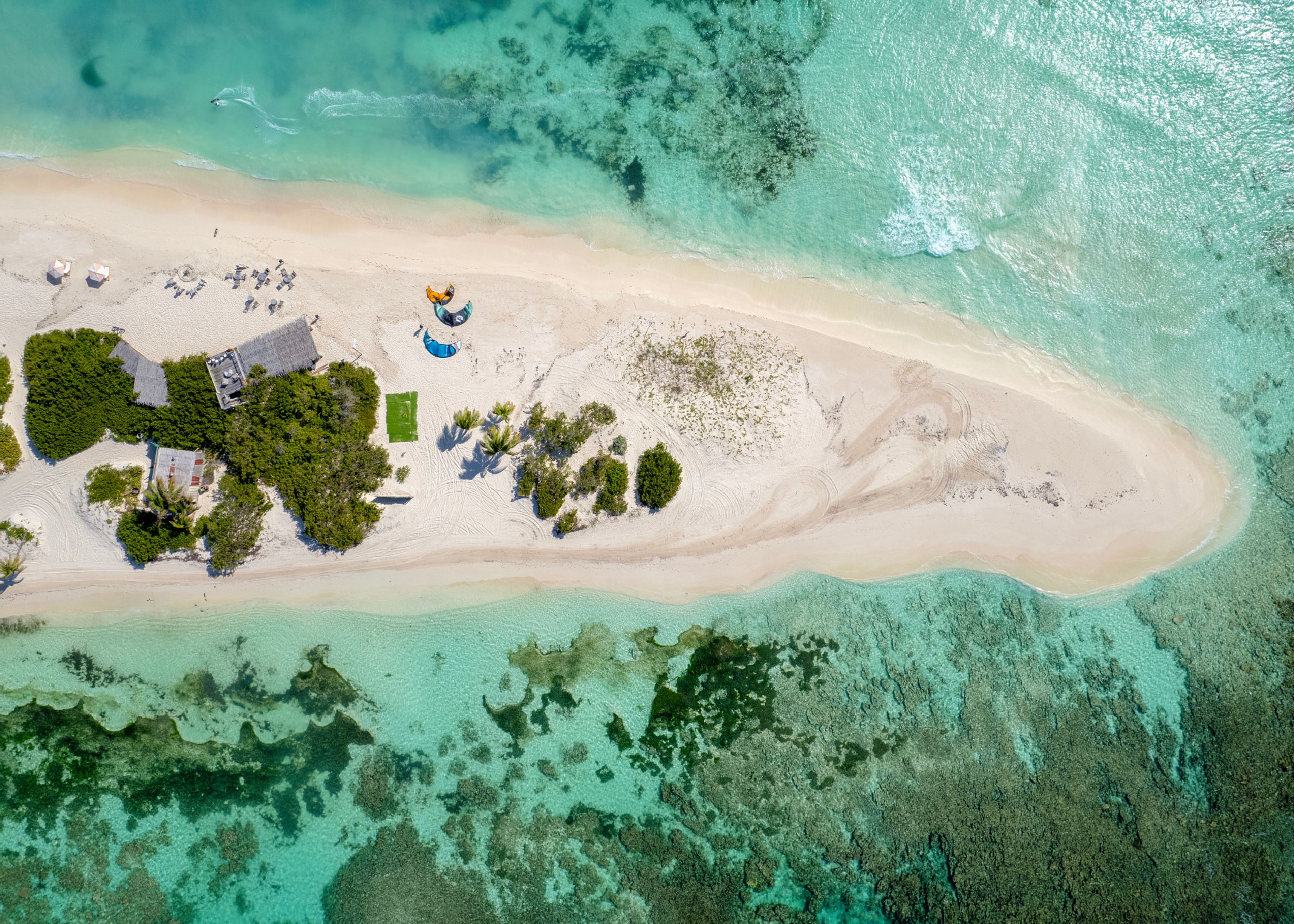 Vista aérea de una isla tropical con playa de arena, aguas turquesas cristalinas y vegetación dispersa.