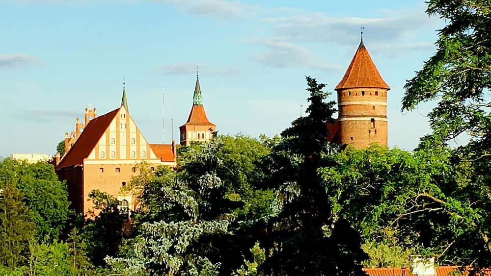 Un château historique doté de nombreuses tours et d’un imposant bâtiment à toit rouge, le tout entouré d’une végétation luxuriante.