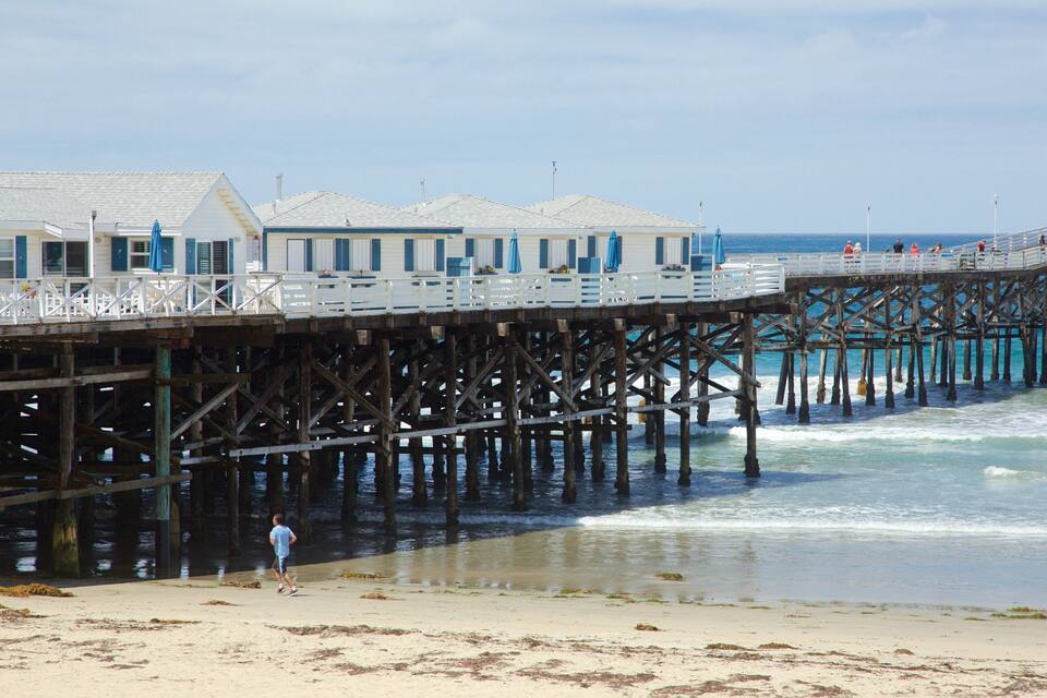 Un muelle que se adentra en el océano, con casas de playa a la izquierda.
