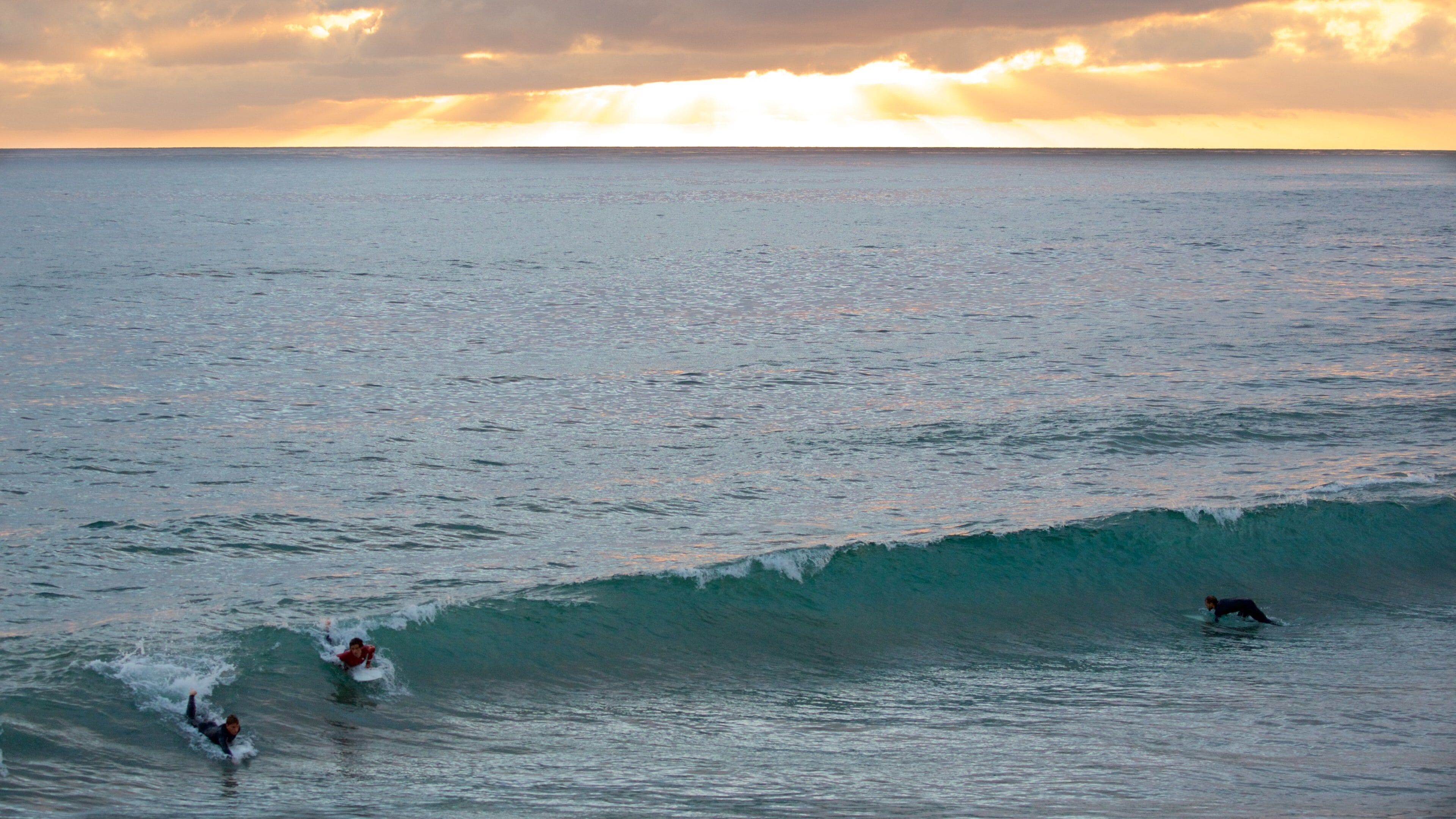 Un atardecer sobre el océano con surfistas montando olas.
