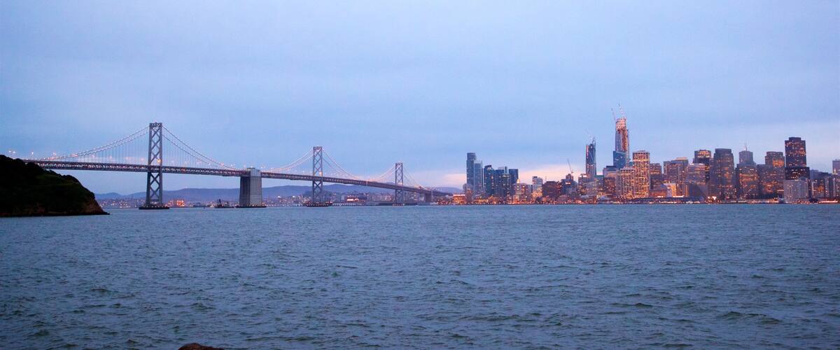 A bridge spanning a body of water with a city skyline in the background.