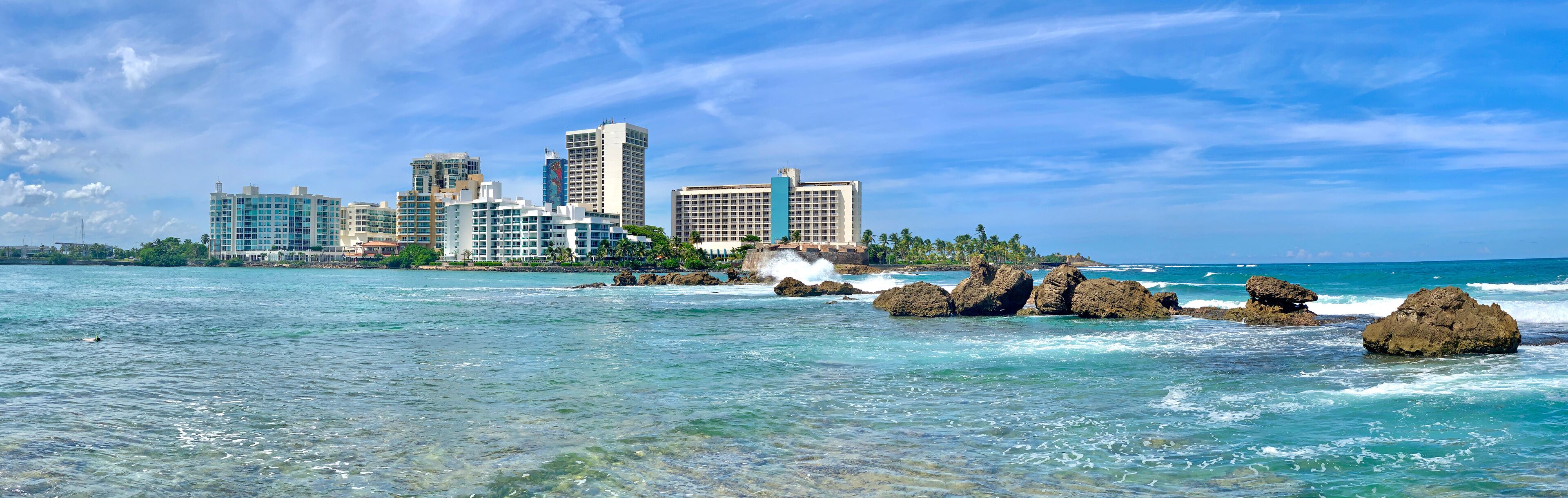 A coastal cityscape with clear blue waters and rocky outcrops.