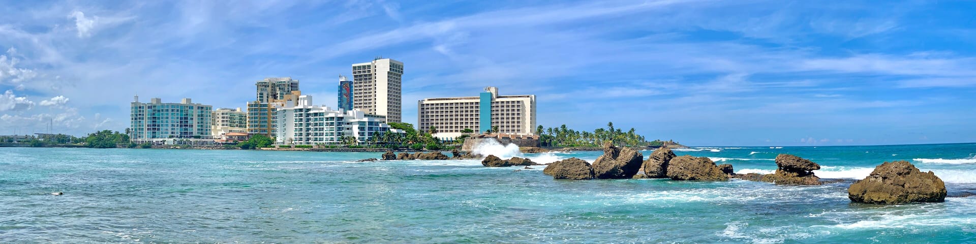 A coastal cityscape with clear blue waters and rocky outcrops.