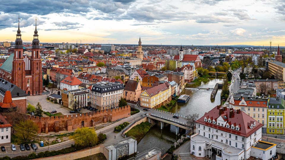A panoramic view of a historic city with prominent red-brick buildings, a river, and a bridge.