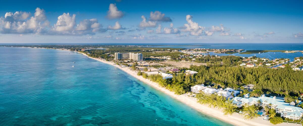 A coastal town with a beach, clear blue waters, and a large hotel complex.