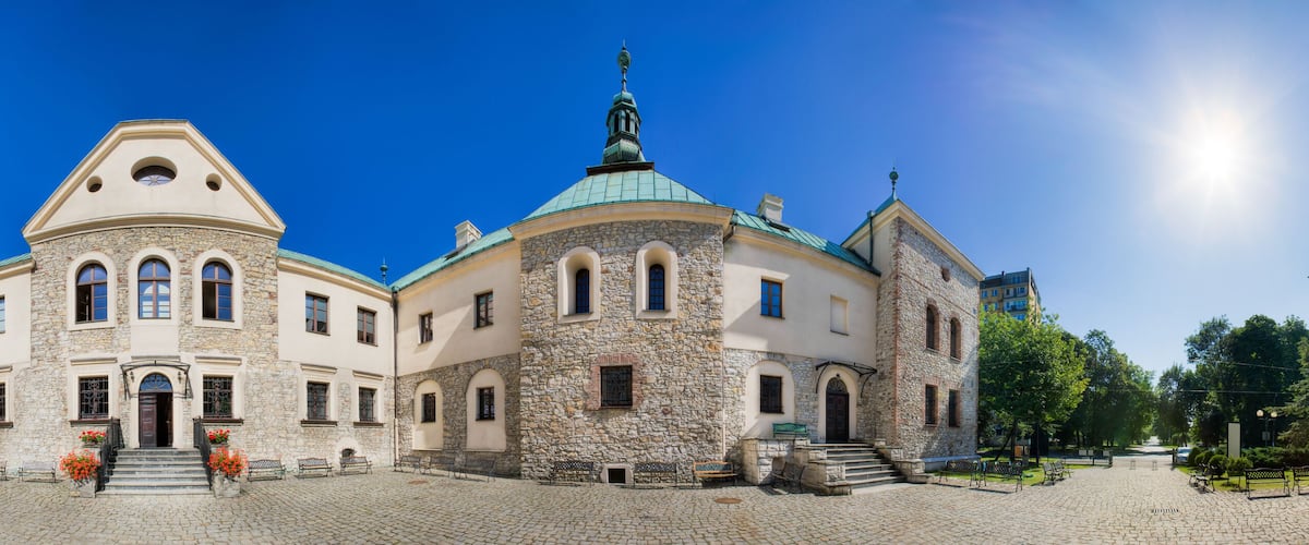 A historic building with a stone facade and a green dome, surrounded by cobblestone streets and benches.
