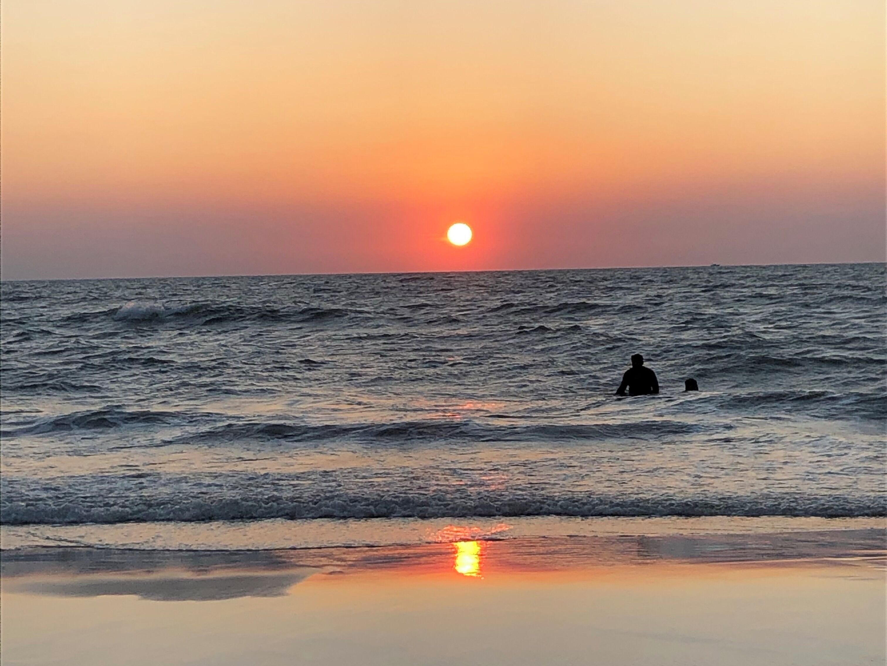 A sunset over the ocean with waves and a person in the water.