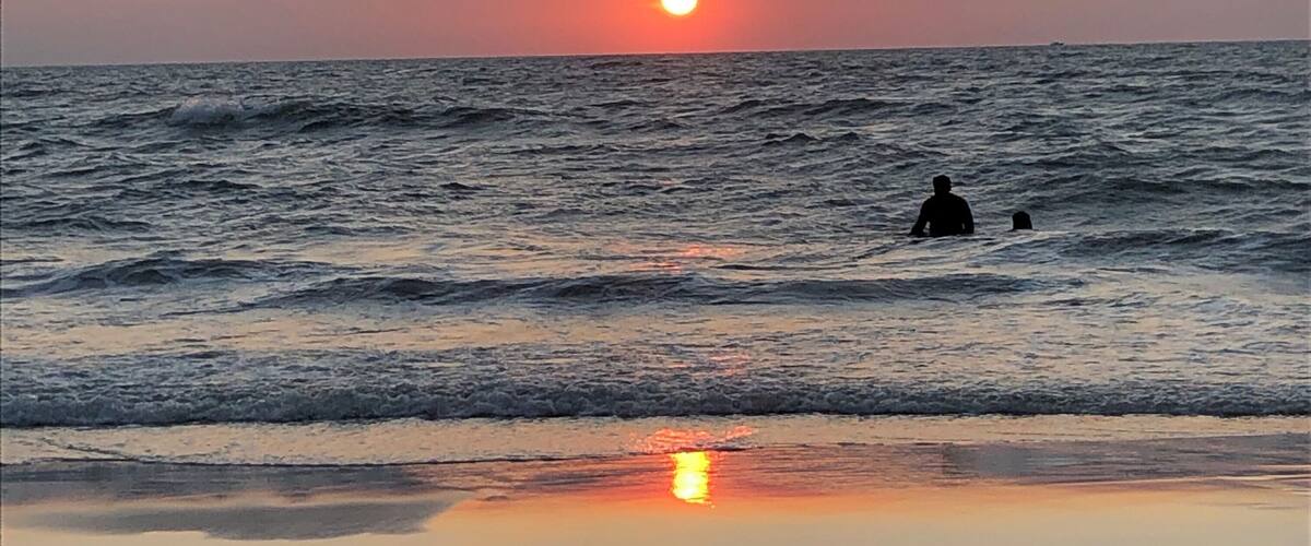 A sunset over the ocean with waves and a person in the water.
