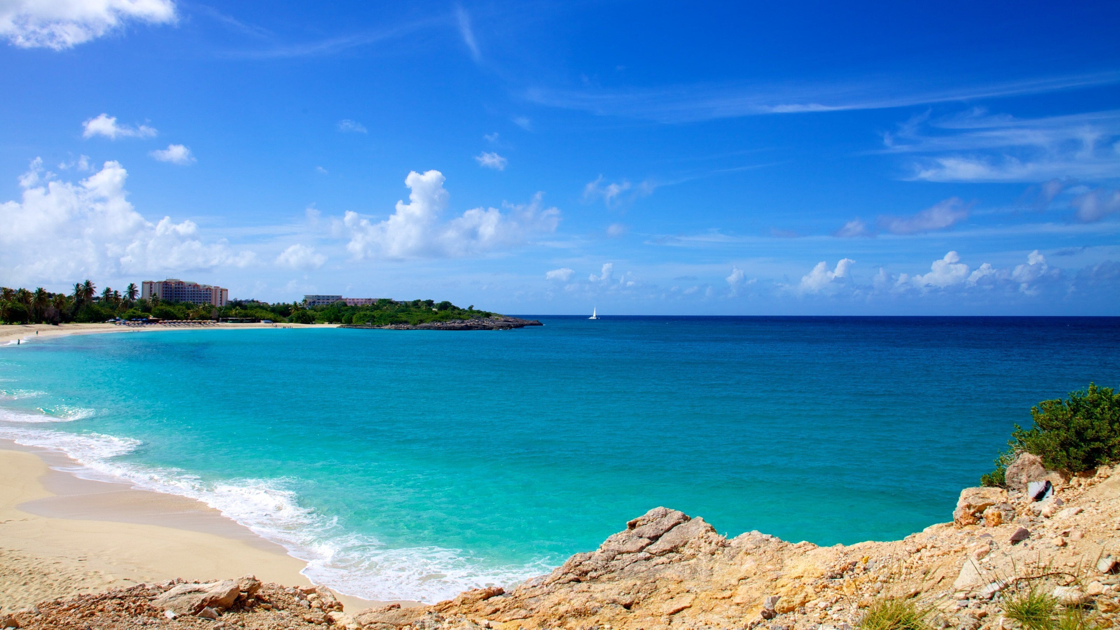A turquoise beach with clear skies and a distant sailboat.