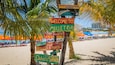 A beach signpost with multiple signs, including 'Welcome to Mullet Bay' and 'St. Maarten D.W.I.'