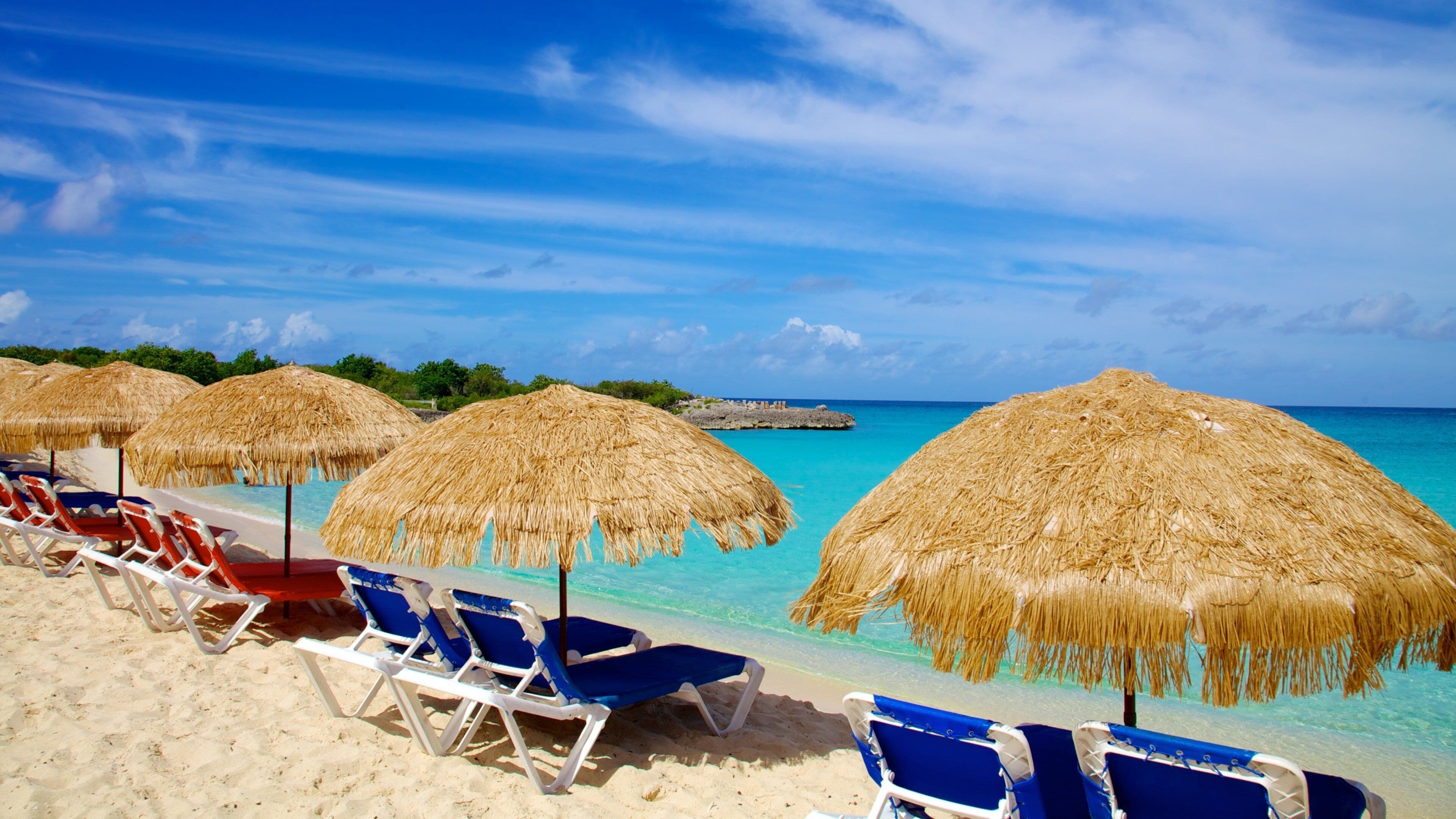 A beach with thatched umbrellas and blue lounge chairs.