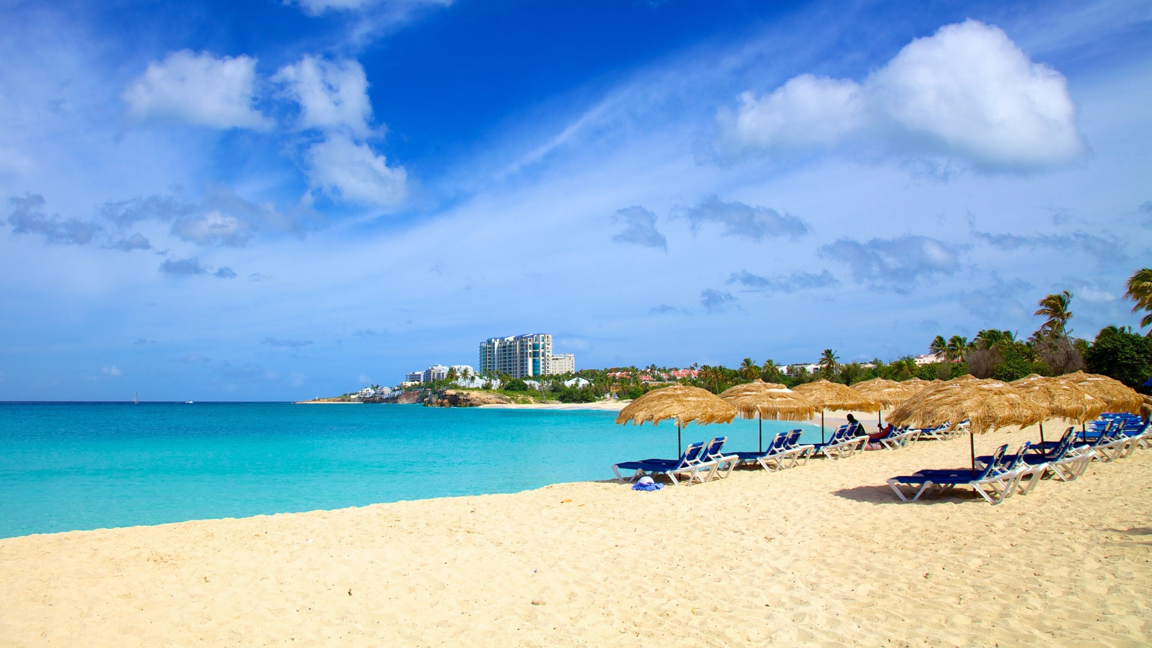 A beach with clear turquoise water, a sandy shore, and a resort with overwater bungalows in the background.