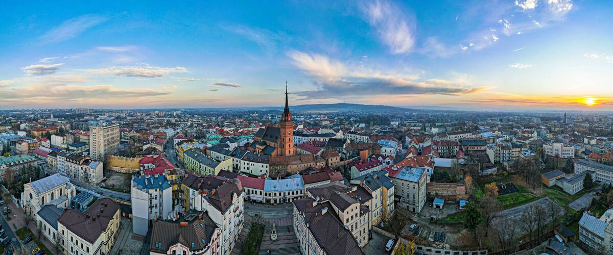 A panoramic view of a cityscape with a prominent church tower and a sunset in the background.