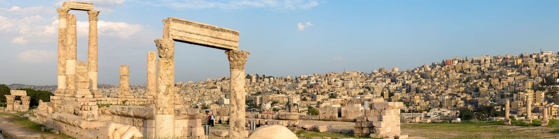 Ancient ruins with columns and a stone archway, set against a cityscape.