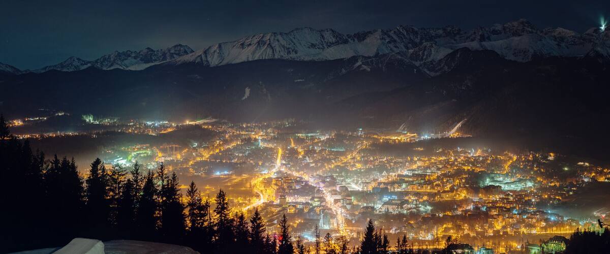 A nighttime view of a town nestled in a valley with snow-capped mountains in the background.