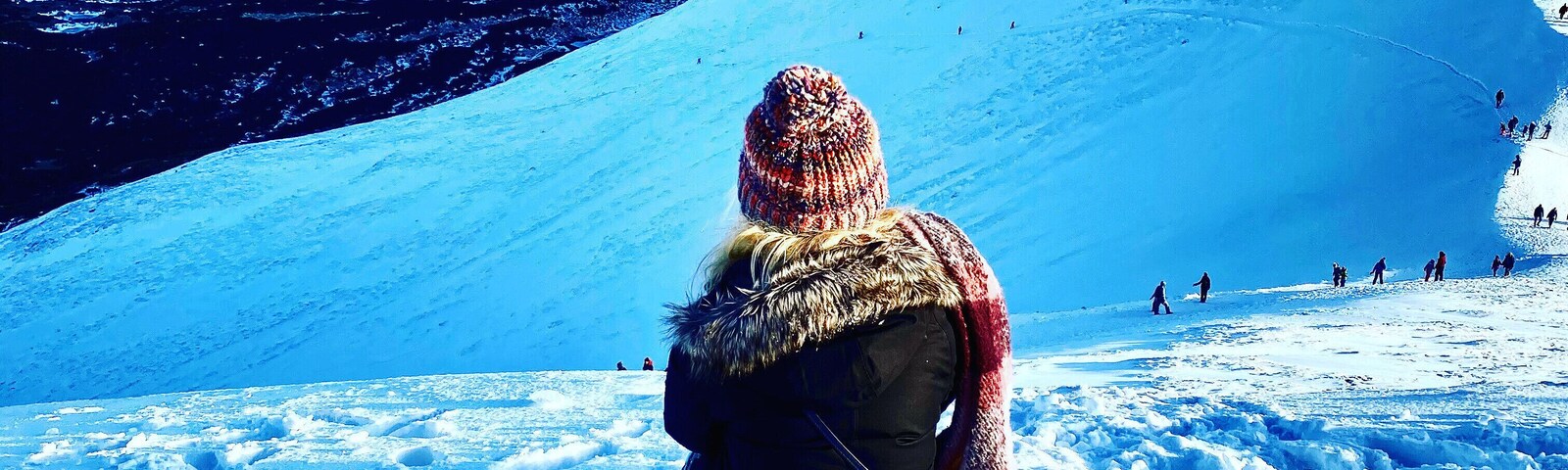 Una persona sentada sobre tierra cubierta de nieve, con una cadena montañosa al fondo.