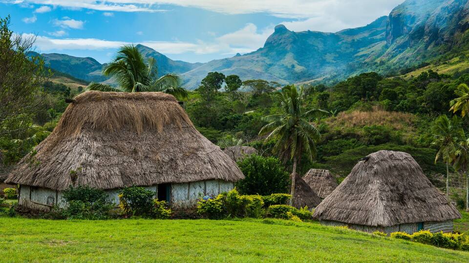 Thatched-roof huts in a lush green valley with mountains in the background.