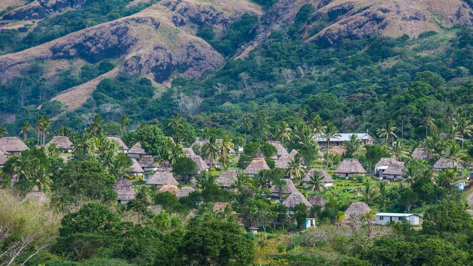A village with thatched-roof houses surrounded by lush greenery and hills.