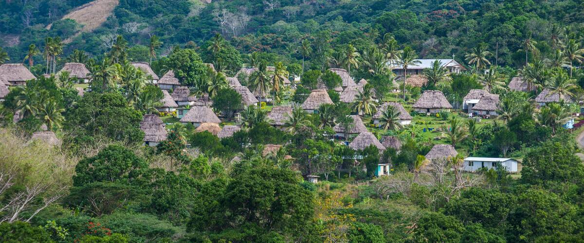 A village with thatched-roof houses surrounded by lush greenery and hills.