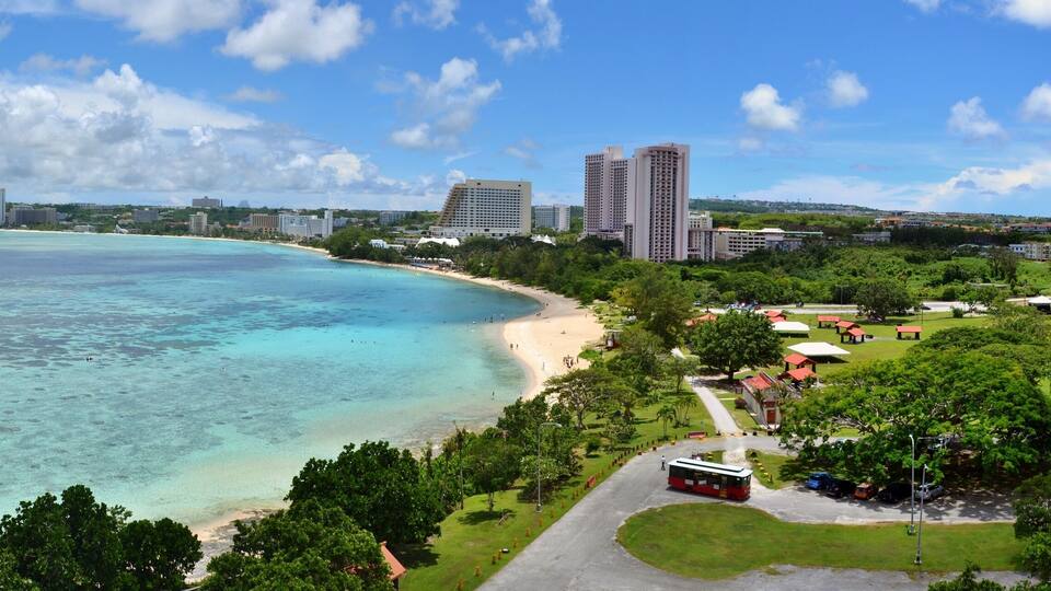 A coastal cityscape with a beach, green park, and high-rise buildings.