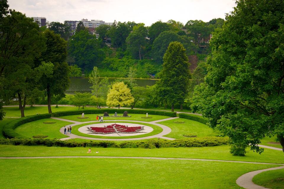 A park with a circular flower bed, trees, and a lake in the background.