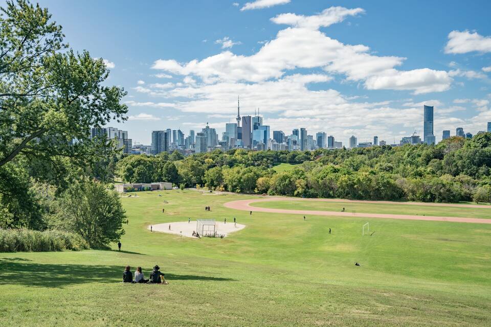 A park with a running track, trees, and a city skyline in the background.
