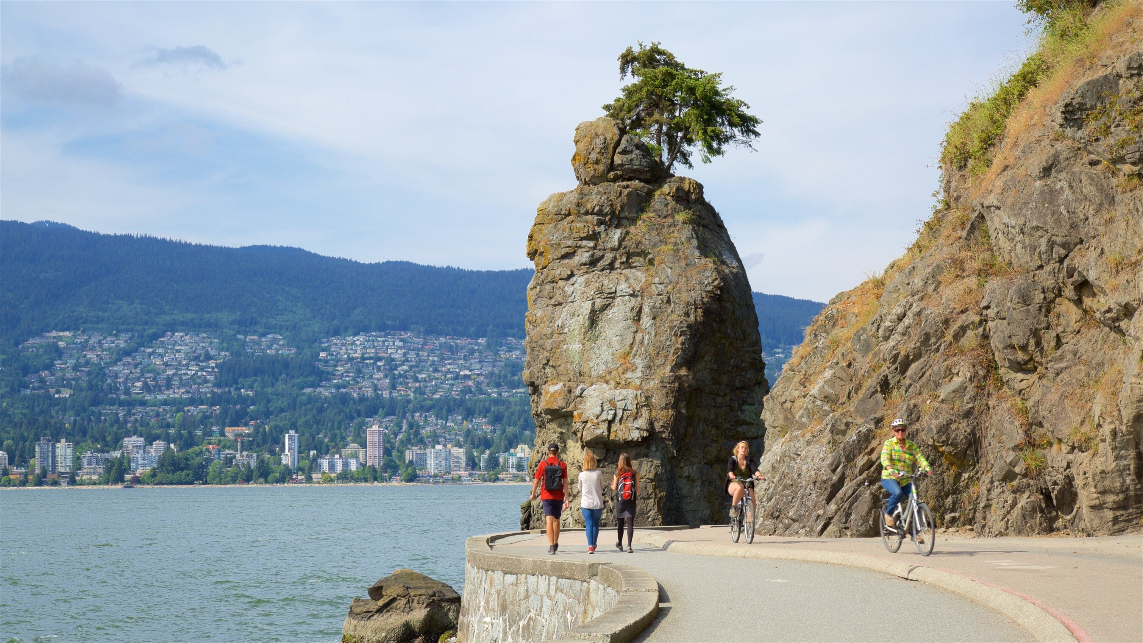 A coastal path with a prominent rock formation and a cityscape in the background.