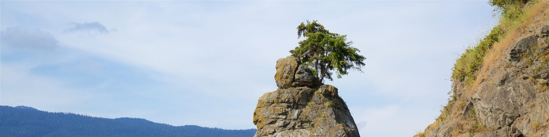 A coastal path with a prominent rock formation and a cityscape in the background.