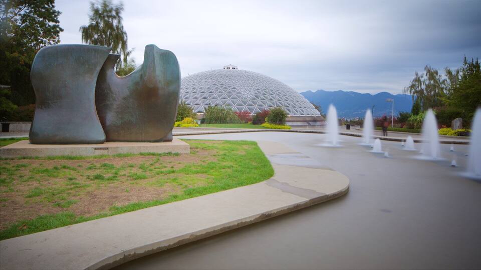 A modern sculpture, a large dome structure, and a fountain in a landscaped area with mountains in the background.
