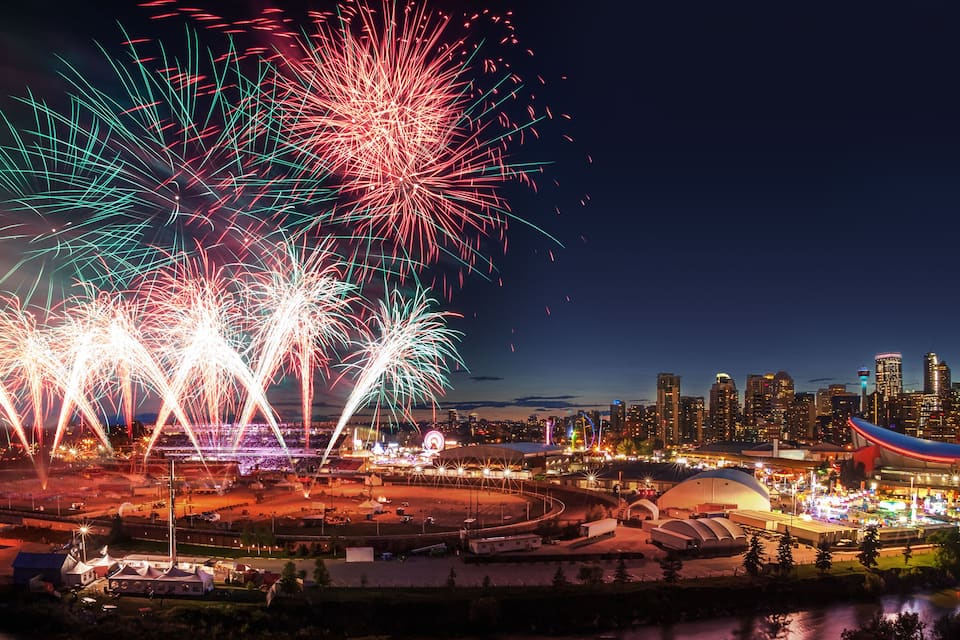 Horizonte urbano com um edifício de arquitetura curva marcante, exibição de fogos de artifício e uma roda gigante.