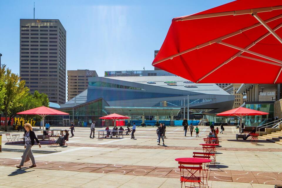 A public square with red umbrellas, outdoor seating, and modern buildings in the background.