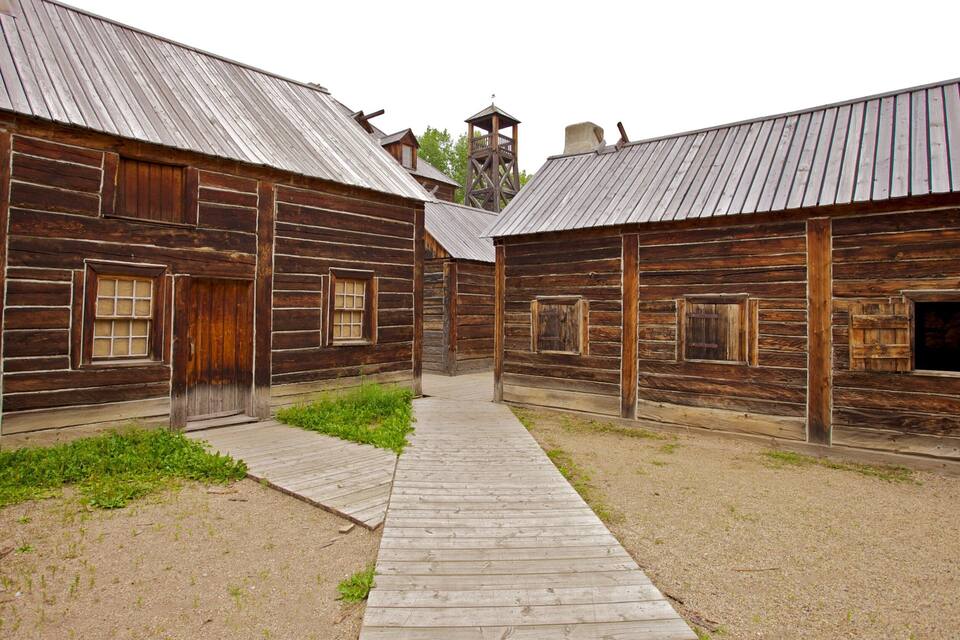 A rustic wooden building with a metal roof and a wooden walkway leading to a central tower.