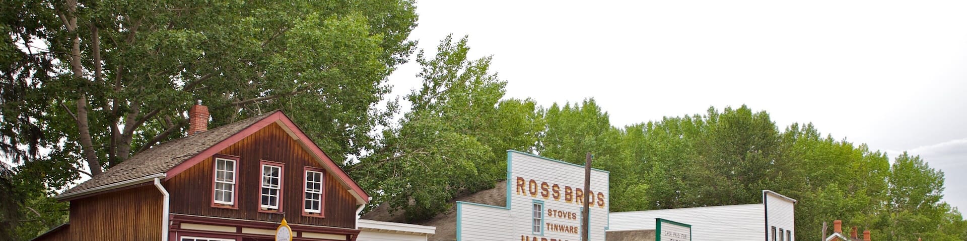 A historic town with wooden buildings, including a hardware store and a Ross Bros store.