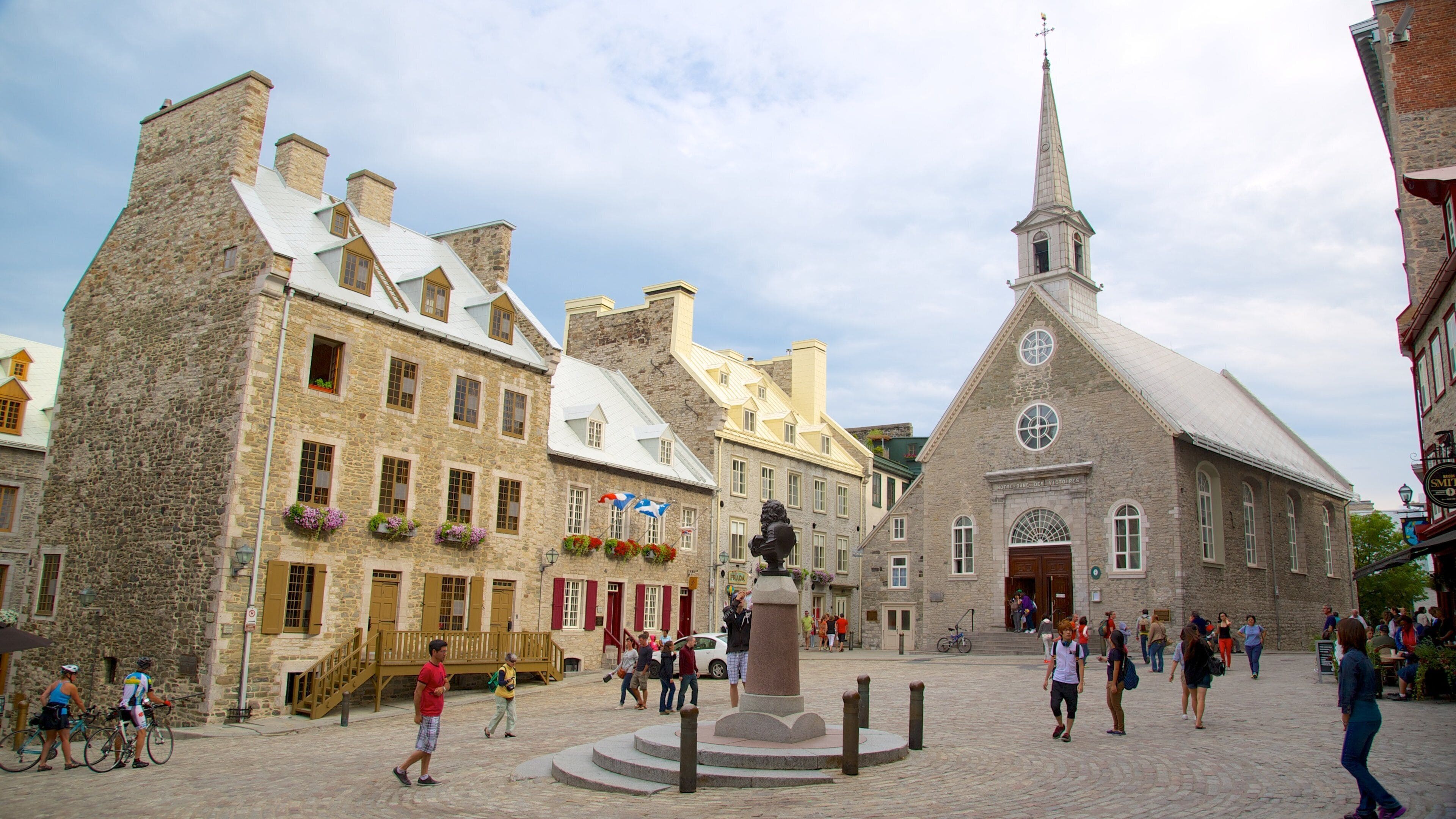 A historic town square with stone buildings, a church, and a statue.