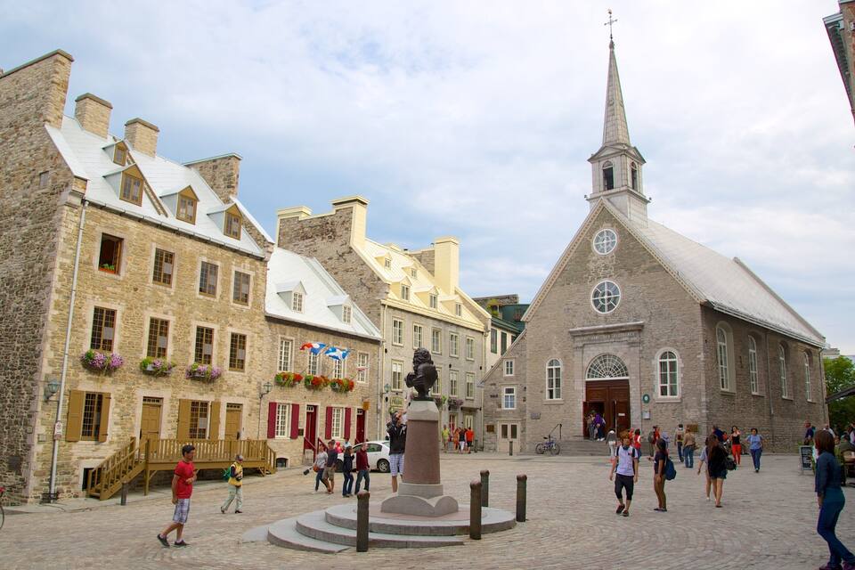 Une place historique bordée de bâtiments en pierre, d’une église et d’une statue.