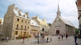 A historic town square with stone buildings, a church, and a statue.
