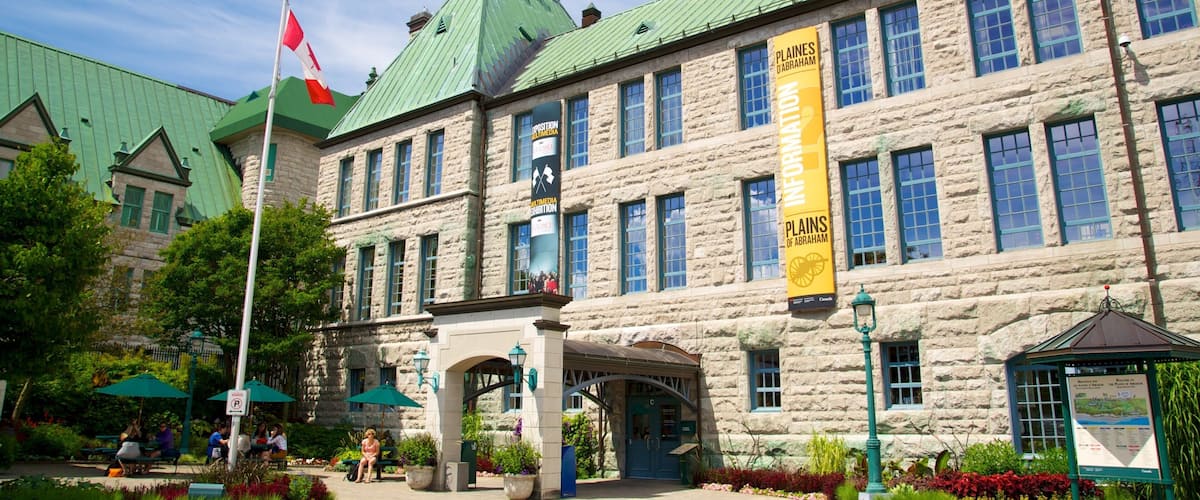 A historic stone building with a green roof, a Canadian flag, and banners advertising an exhibition.