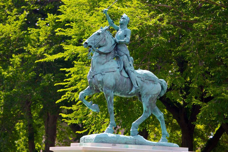 Una estatua ecuestre de bronce en un parque, con árboles verdes y frondosos al fondo.