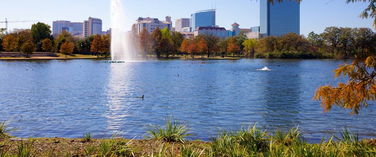 Fountain splashes in serene Hermann Park with Houston skyline backdrop during a sunny afternoon