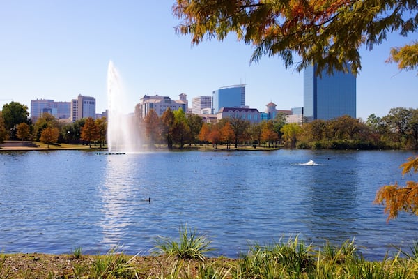 Fountain splashes in serene Hermann Park with Houston skyline backdrop during a sunny afternoon
