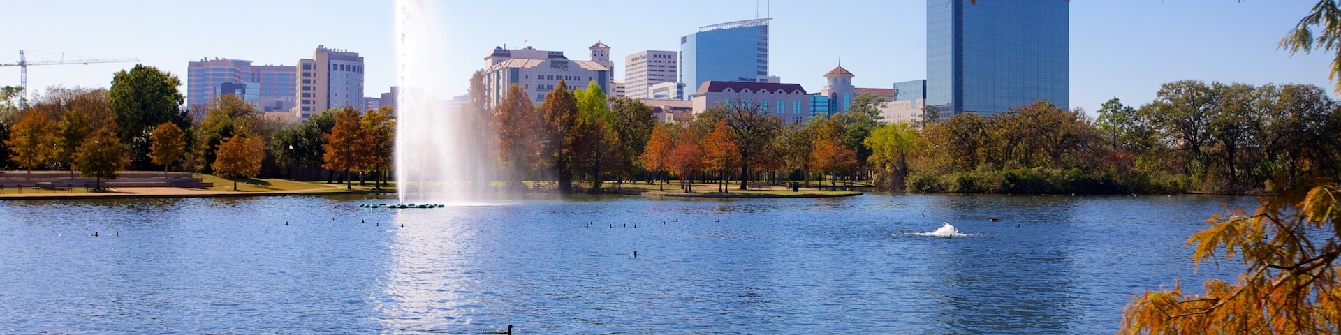 Fountain splashes in serene Hermann Park with Houston skyline backdrop during a sunny afternoon