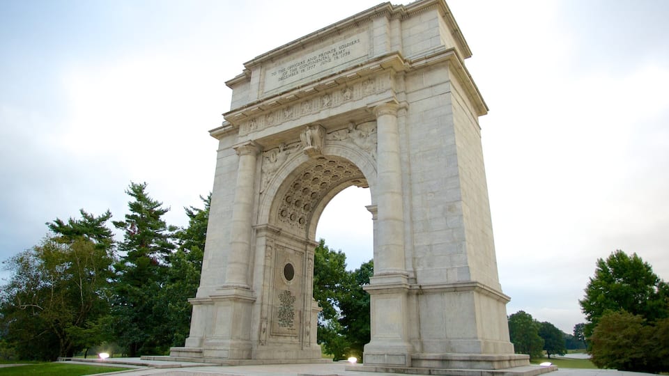 A large stone arch monument with inscriptions, surrounded by trees and a grassy area.