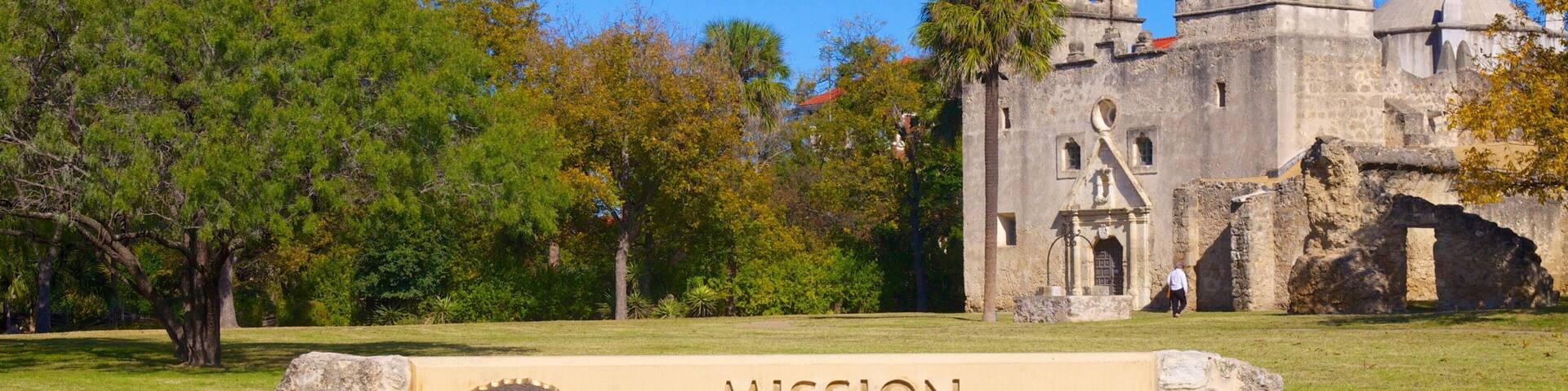 A historical building with a bell tower, surrounded by trees and a sign for the Mission Concepcion National Historical Park.