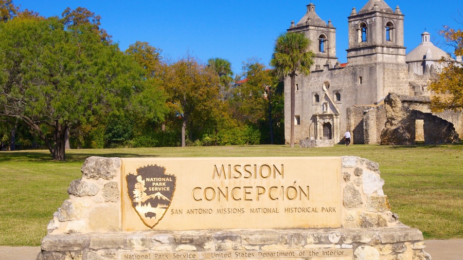 A historical building with a bell tower, surrounded by trees and a sign for the Mission Concepcion National Historical Park.